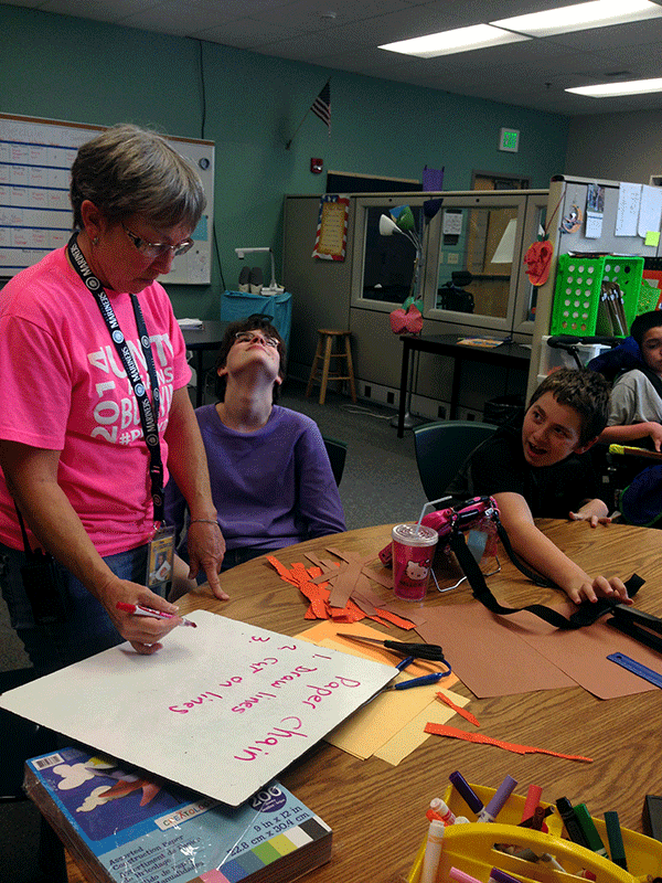 Rhyann Morgan (9) and Erik Johnson (9) help Para-educator Mrs. freeman write directions on how to make a paper chain. during 6th period, Morgan and Johnson stay in the classroom to work on craft projects, while other students go to the gym and do other activities. 