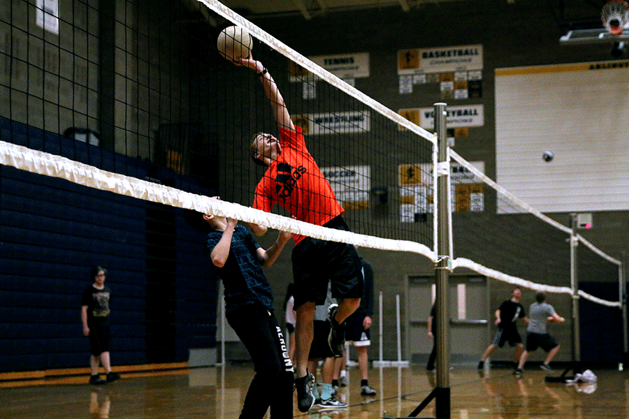 A student goes up to spike the ball while playing volleyball in Net Sports.