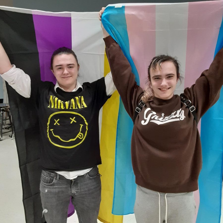 Pine Osborne (left) and Jessica Slavick stand donning the flags of their respective gender identities. Osborne is pictured with the non-binary flag, and Slavick with the transgender flag.