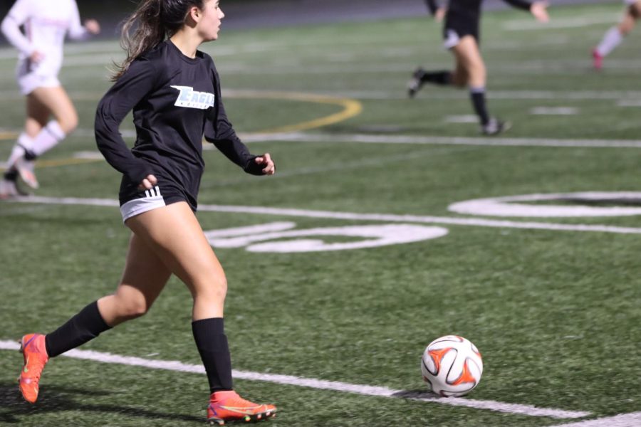 An AHS Soccer play moves the ball down the field followed closely by both her teammates and the opponent.