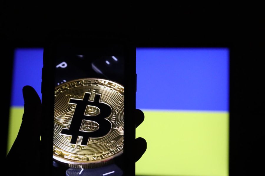 A novelty physical bitcoin is seen on a phone screen silhouetted by the Ukrainian flag. 