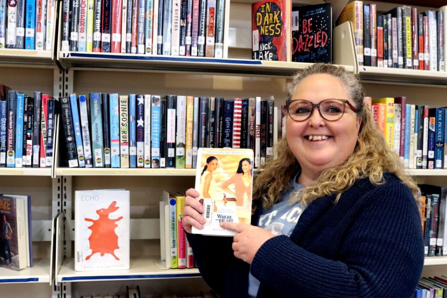 Ms. Muniz, High School Librarian, is posing next to her favorite shelf in the library with her favorite book. Ready to share on social media to give inspiration to other readers. 
