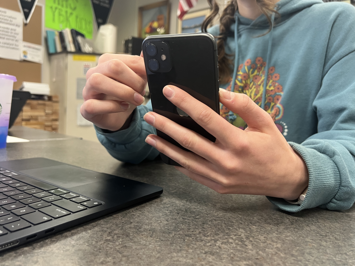 Student holding phone, while researching on computer.