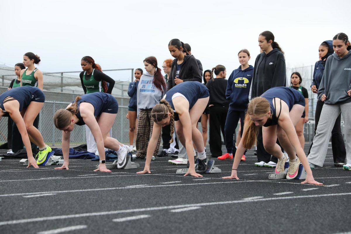 Late march track meet at John C Larson Stadium, lining up for the 100m dash. In lane one Kylee Russell (27), in lane two Kenna Langford (28), in lane three Sophia Muzzy (28), and in lane four Peach Hunter (27). 